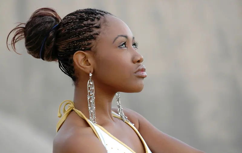 Elegant portrait of a woman with braided hair and stylish earrings looking thoughtful against a neutral background.