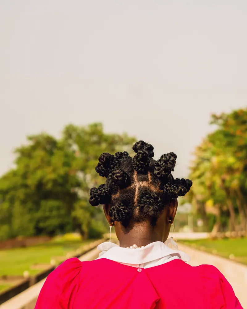 Person with Bantu knots in a red shirt enjoying a sunny day outdoors.