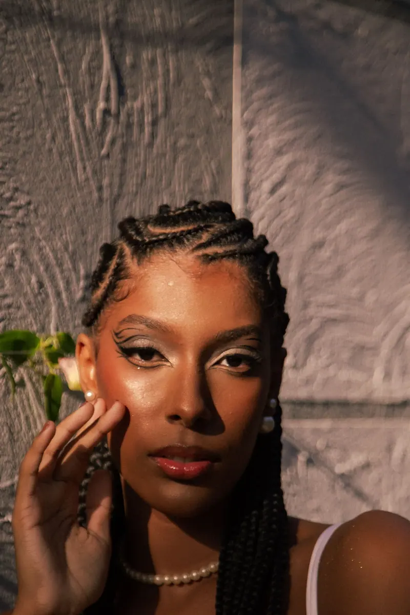 Elegant portrait of a woman with braided hair and bold makeup under sunlight.