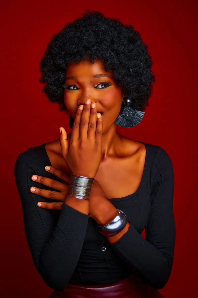 Elegant portrait of a smiling woman with afro hair against a rich red background.