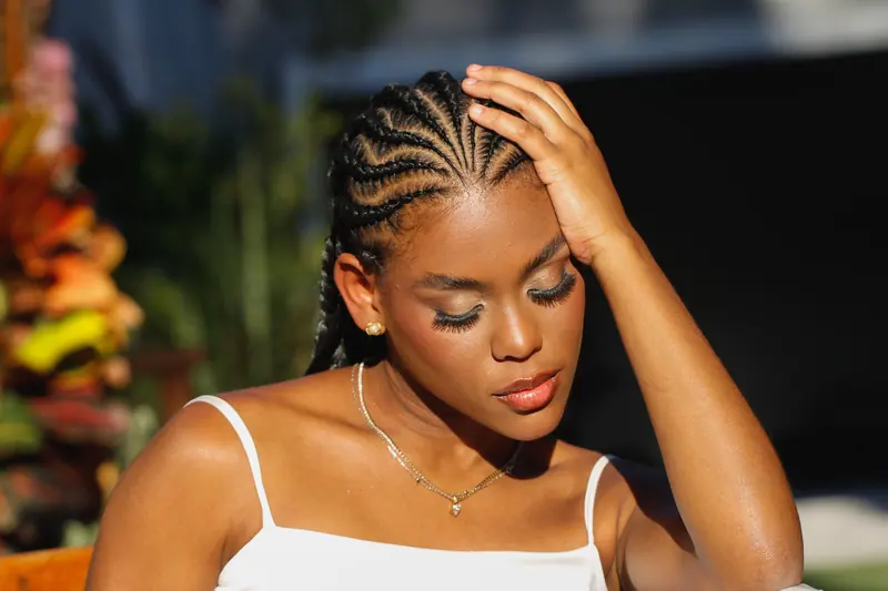 A woman in summer attire with braided hair, basking in sunlight.