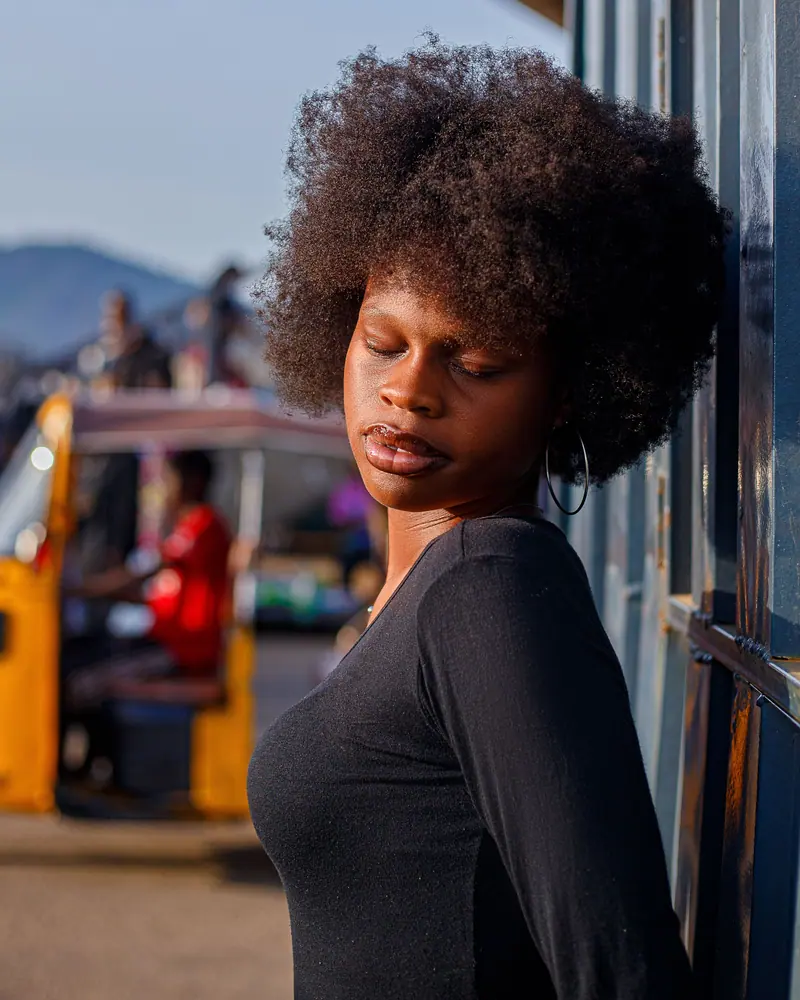 Young woman with afro hairstyle leans against a wall in a vibrant urban scene during the day.