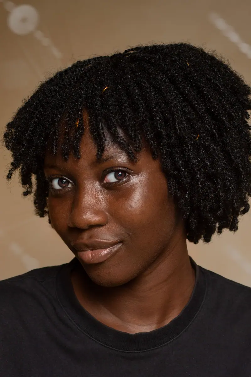A close-up portrait of a woman with natural curls, captivating eyes set against a neutral backdrop.