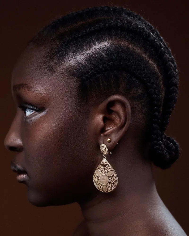 Side profile of a woman with intricate braids and an ornate earring on a dark background.