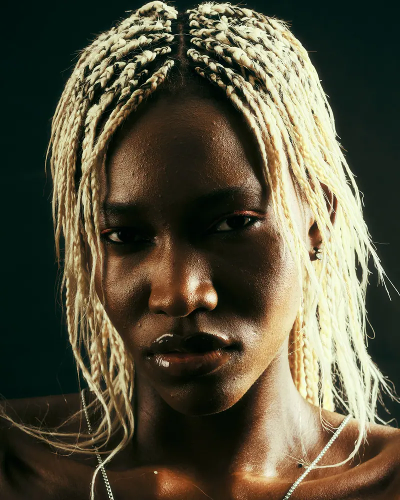 Striking portrait of a black woman with blonde braids, strong expression.