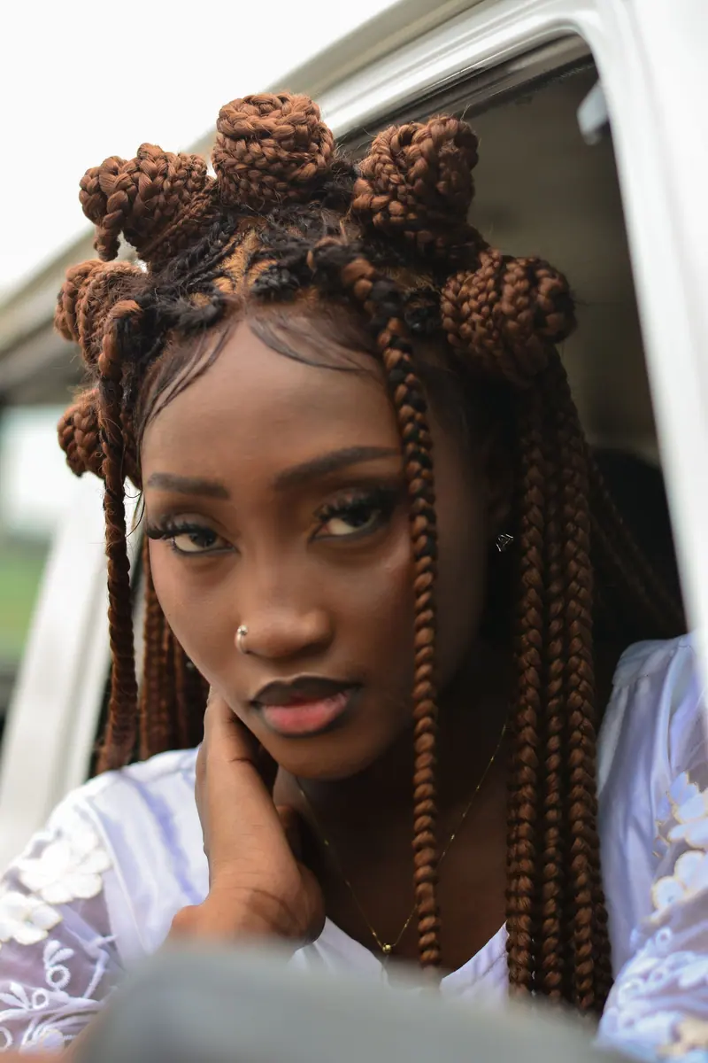 Close-up portrait of a woman with unique braided hair, looking out of a vehicle window.