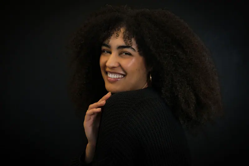 Captivating portrait of a smiling woman with curly hair against a black background.