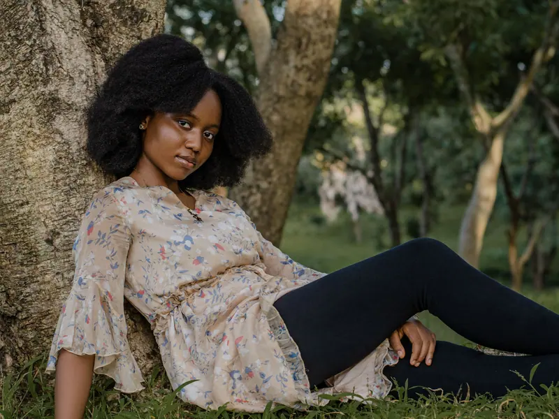 A young woman relaxes under a tree in a serene outdoor setting, capturing a moment of peace and nature.