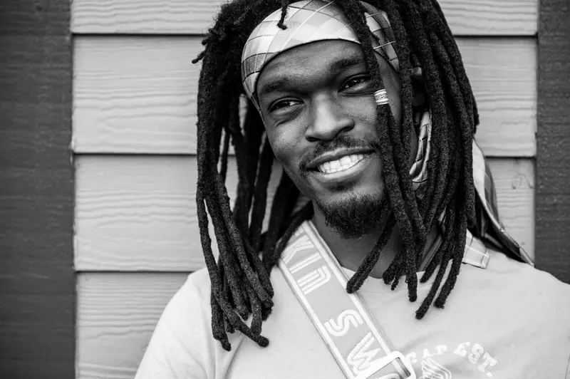 Black and white portrait of a smiling man with dreadlocks and a patterned headband.