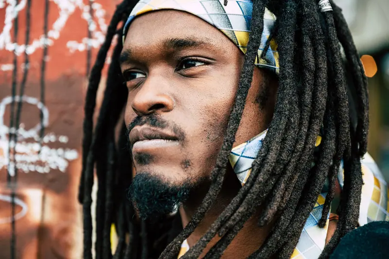 A close-up portrait of a man with dreadlocks and a colorful headband, showcasing fashion and style.
