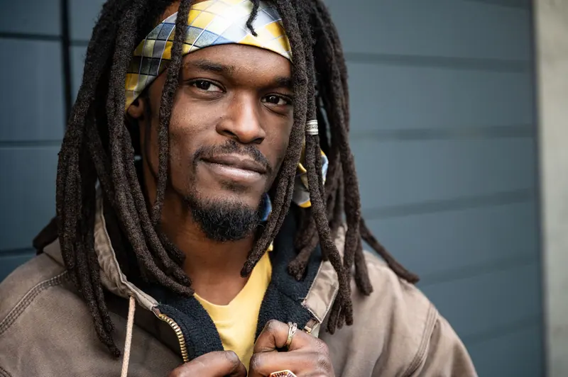 Smiling man with long locs and a canvas jacket