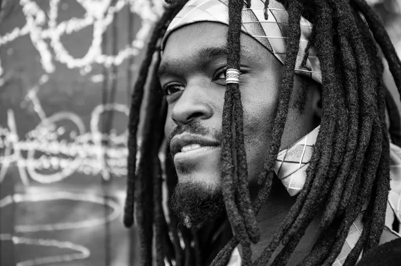 Black and white close-up portrait of a man with dreadlocks and bandana, gazing thoughtfully.