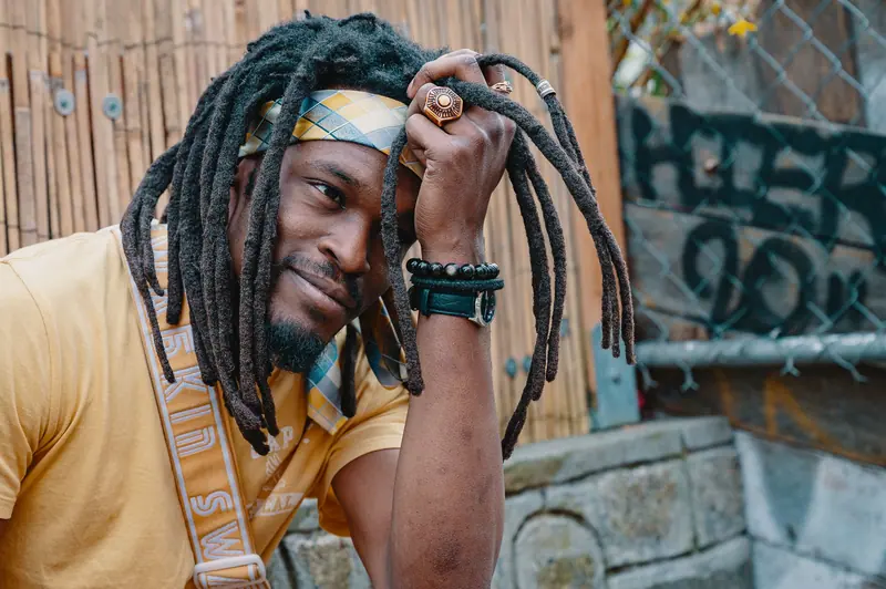 Close-up portrait of a smiling man with dreadlocks in an outdoor urban setting. Unique style and relaxed expression.