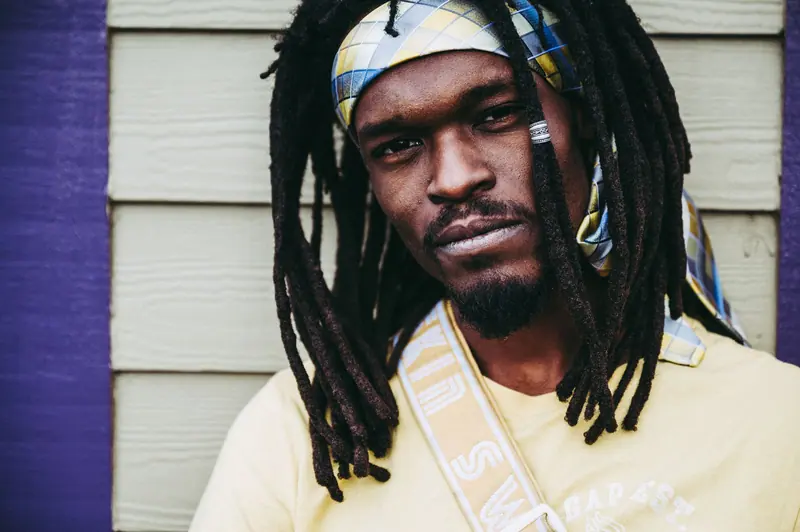 Confident urban male with dreadlocks and colorful headband in a thoughtful pose.