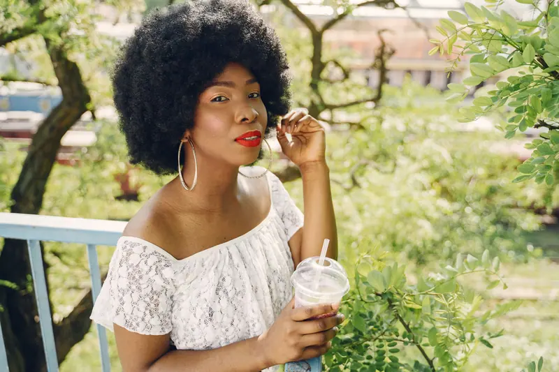 Black woman with afro hair holding a drink in an outdoor setting.