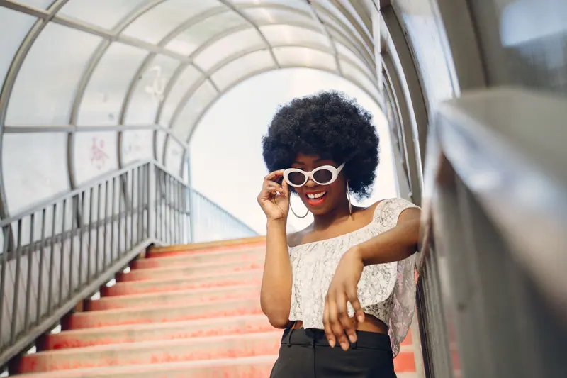 Smiling woman with afro hairstyle wearing sunglasses on a sunny day.