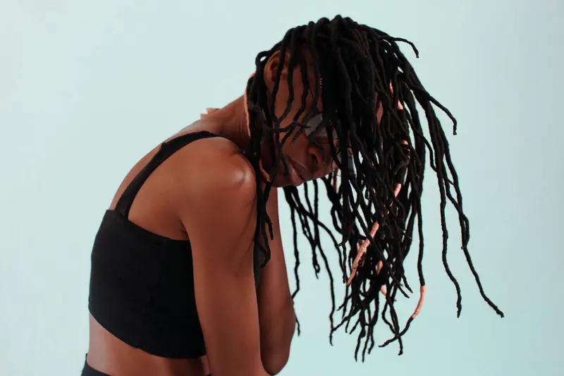 Striking studio portrait of a woman showcasing her dreadlocks against a light blue background.