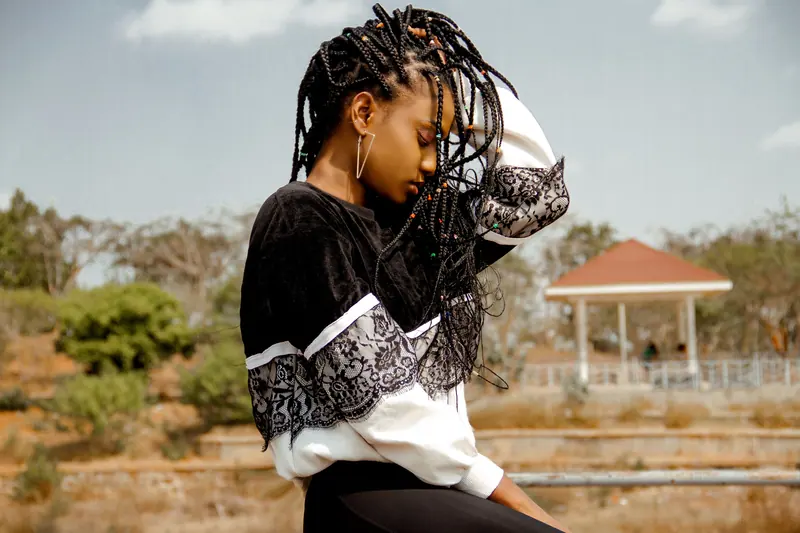 A young woman with braided hair enjoys a serene moment outdoors, embodying style and mindfulness.
