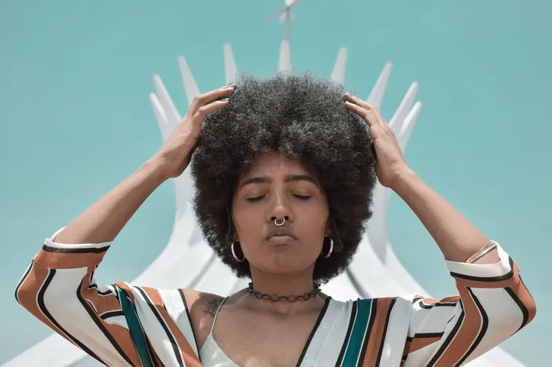 Young woman with afro hairstyle poses outdoors in front of iconic Brasília Cathedral.
