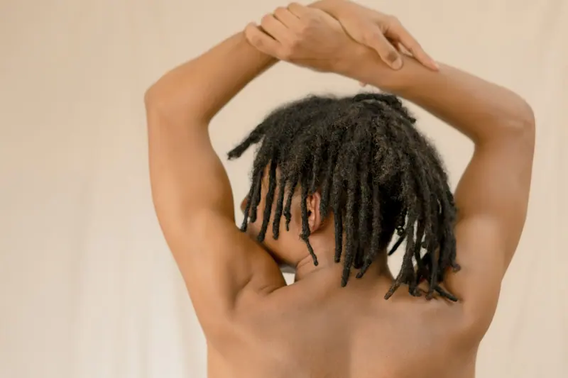 Minimalist nude portrait focusing on arms and back with dreadlocks, embodying strength and freedom.