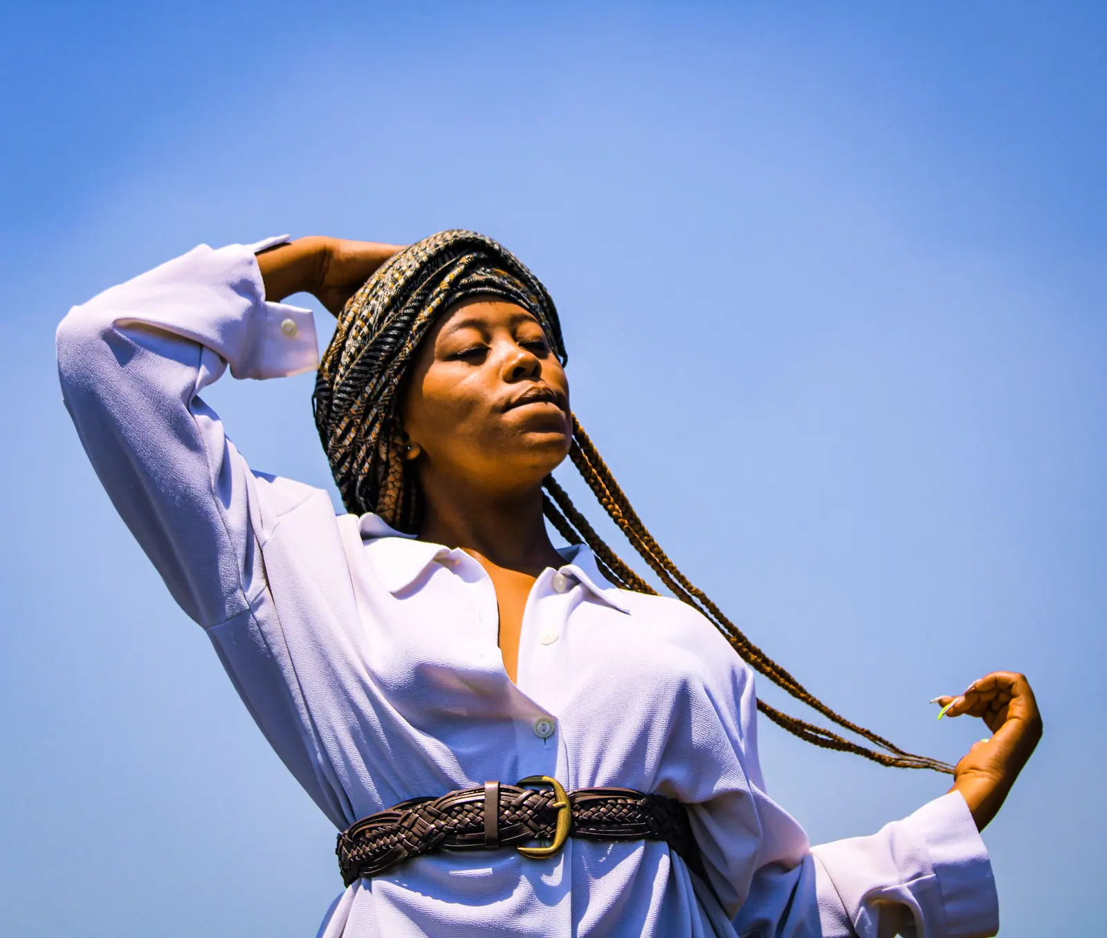 Woman with long braids swinging one braid against a clear blue sky