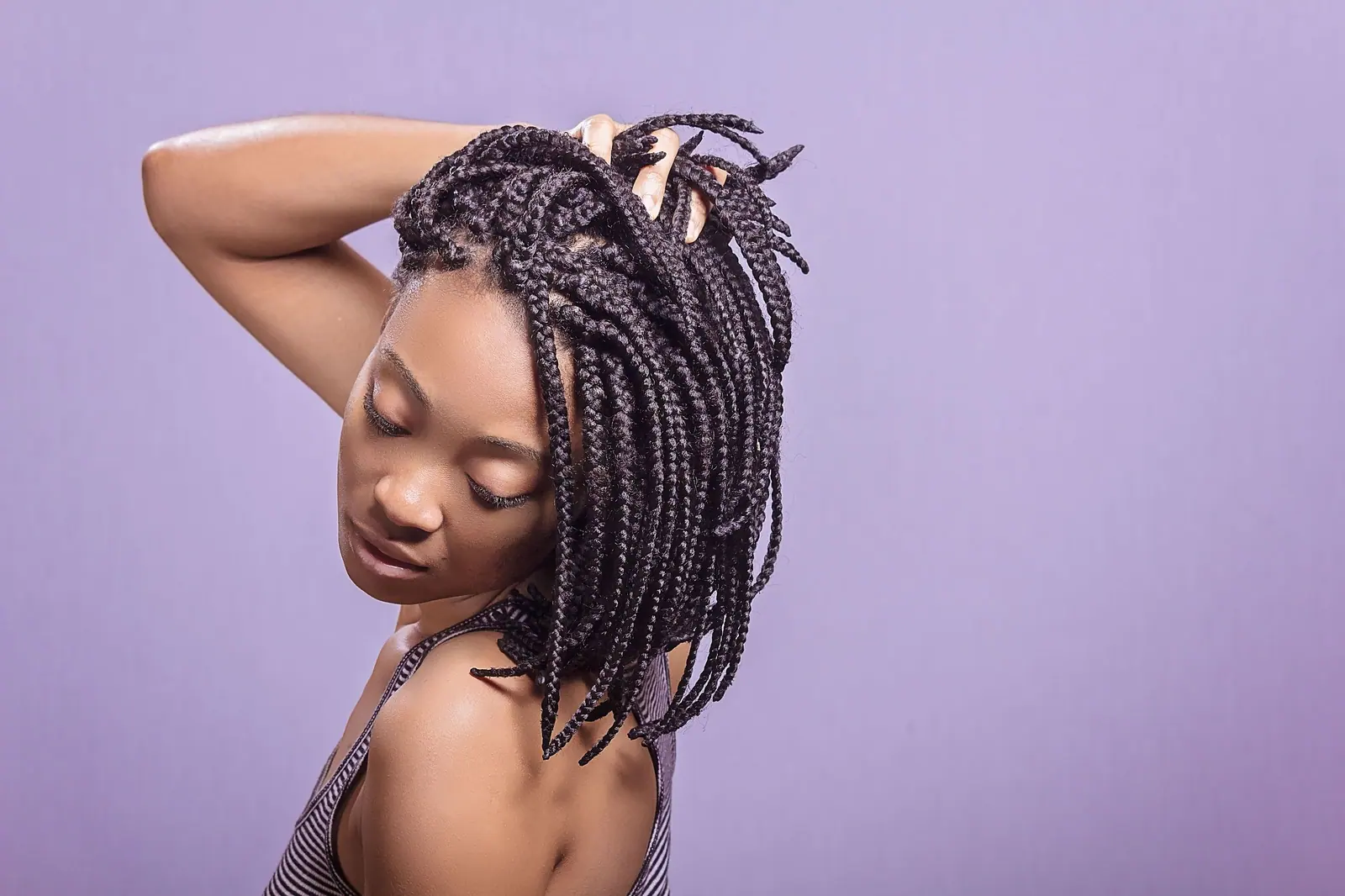 Woman with shoulder-length box braids turning her head against a soft lilac backdrop