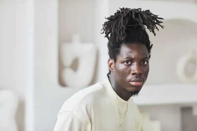 Close-up portrait of a fashionable man with dreadlocks looking intense indoors.