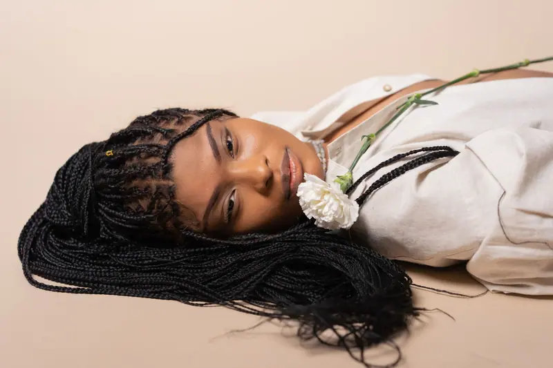Client resting on a peach backdrop, waist-length micro braids fanned around her and a white rose tucked in