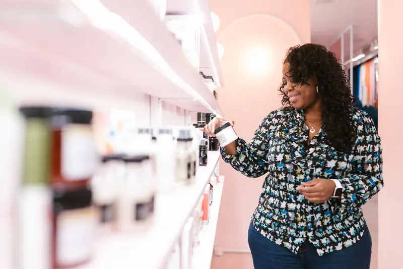 Smiling woman browsing beauty products on store shelves.