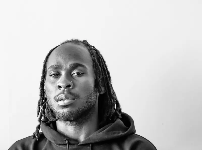 Artistic black and white portrait of a man with dreadlocks against a white background.