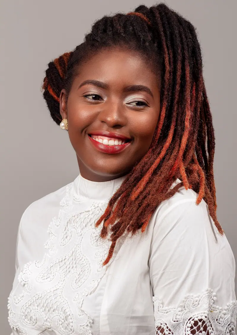 Charming portrait of a young black woman with dreadlocks smiling in a studio setting.
