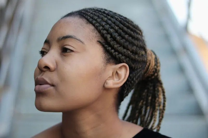 Close-up of a woman with braided hair looking thoughtful outdoors in Durban.