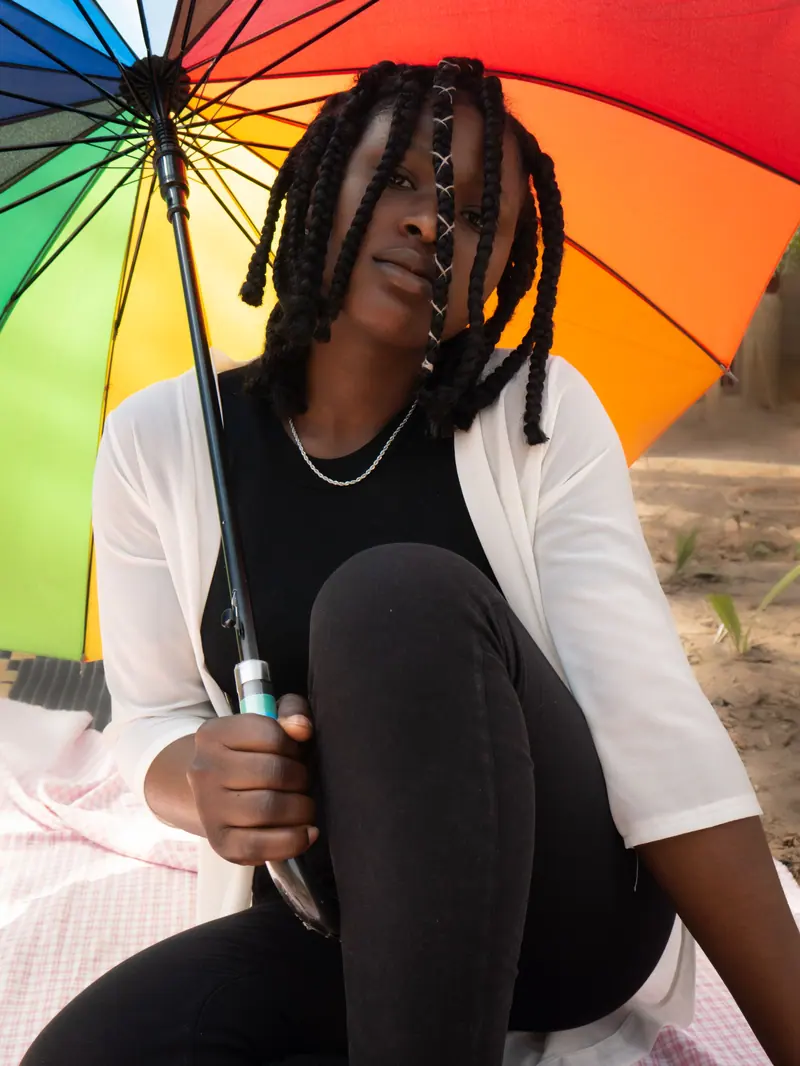 A young woman poses outside with a vibrant rainbow umbrella, embodying summer fashion vibes.