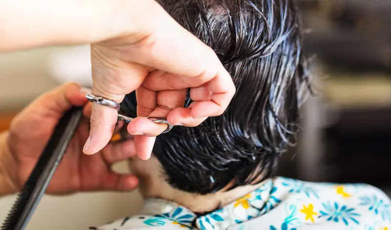 Close-up of a hairstylist cutting short wet dark hair at a salon.