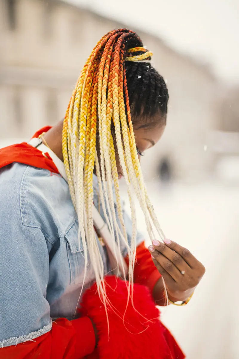 African American woman with vibrant braids poses in snowy urban environment.