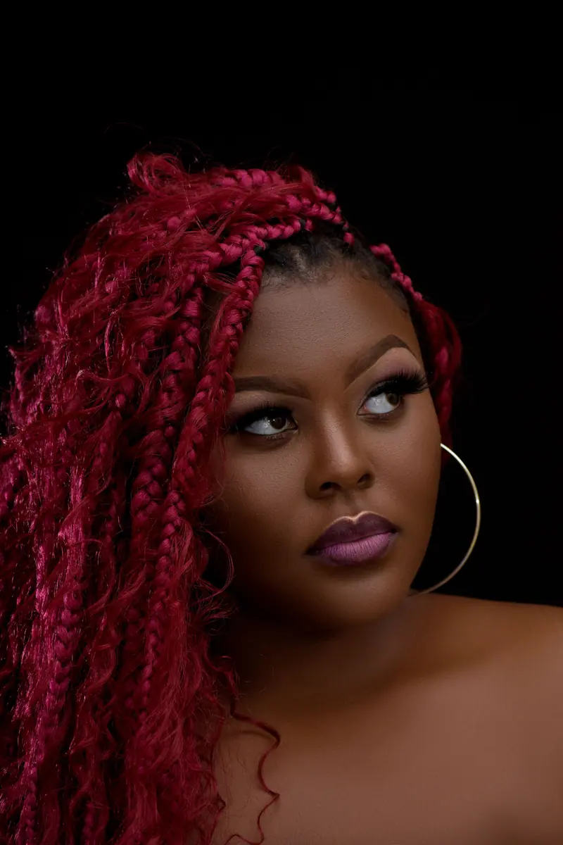 Stunning close-up portrait of a woman with vibrant pink braided hair and hoop earrings on a black background.