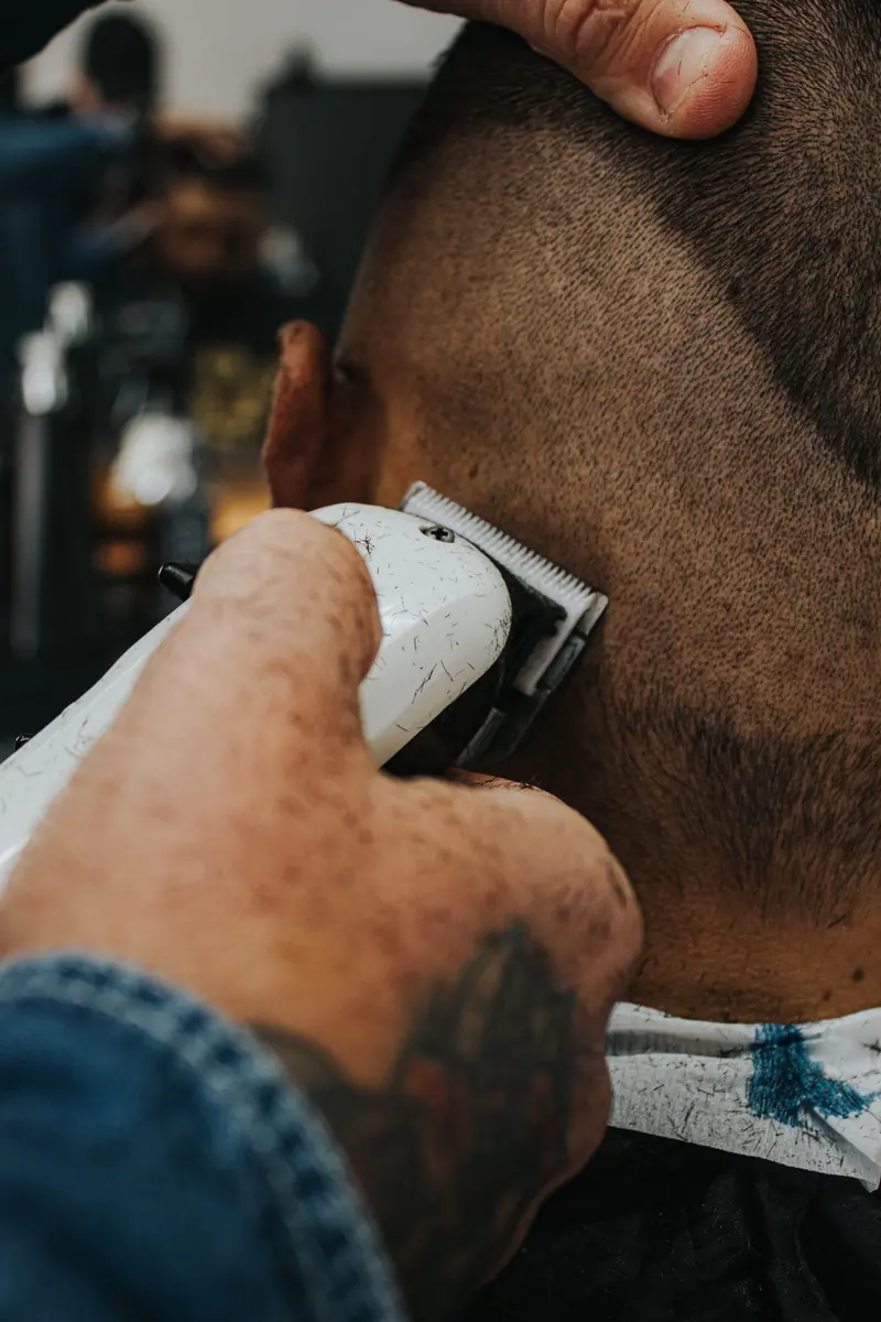 Detailed shot of a barber using clippers on a client's head in a barbershop.