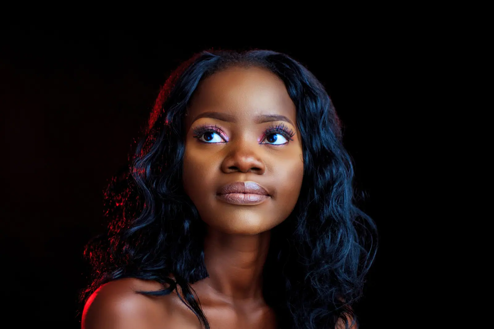 Noelle Marchand, a Black sew-in artist with long blue-black waves, looking up against a dark studio background