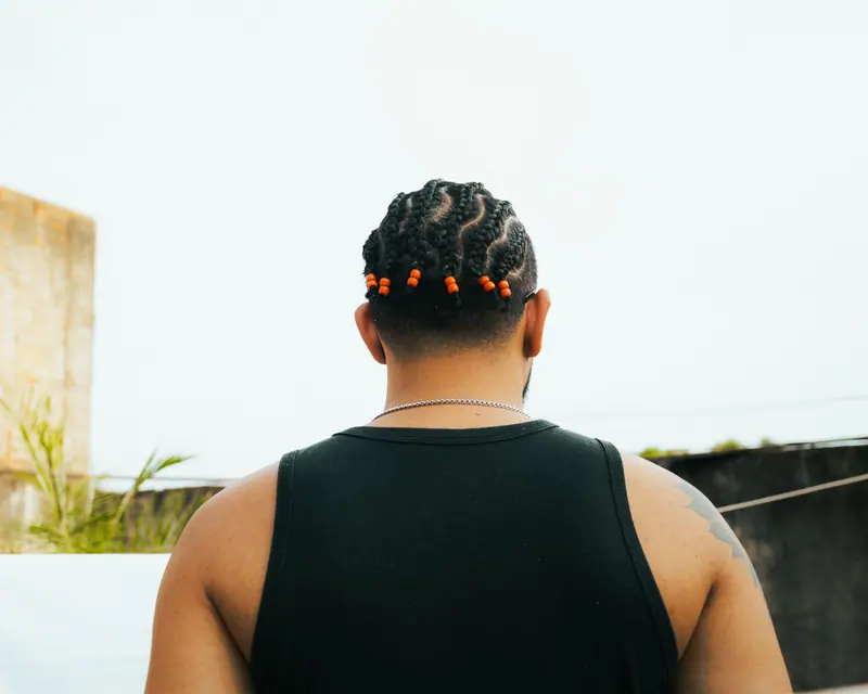 Tattooed man with braided hair stands outdoors in Presidente Prudente, capturing urban life.