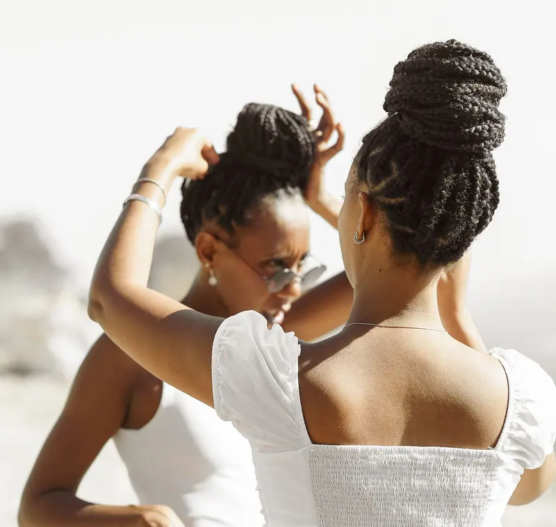 Two women styling hair outdoors, showcasing friendship and elegance on a sunny day.