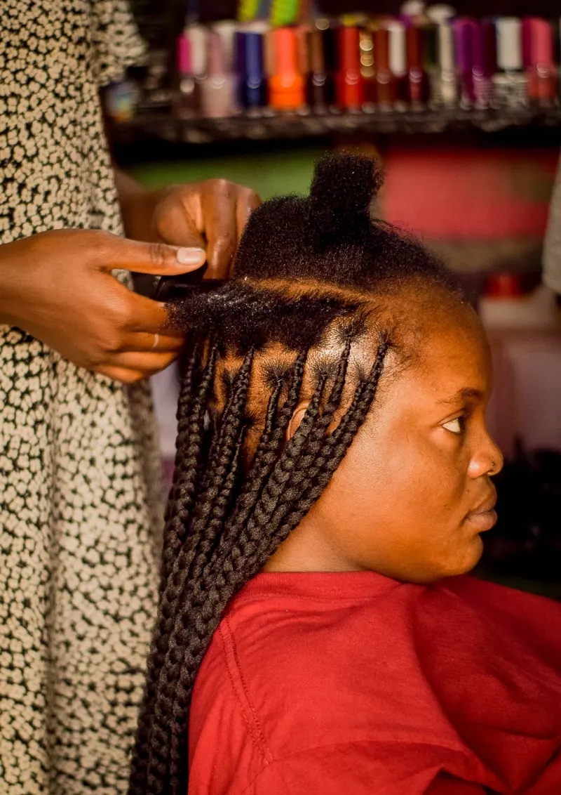 Close-up of an African woman having her hair braided in a colorful salon setting.