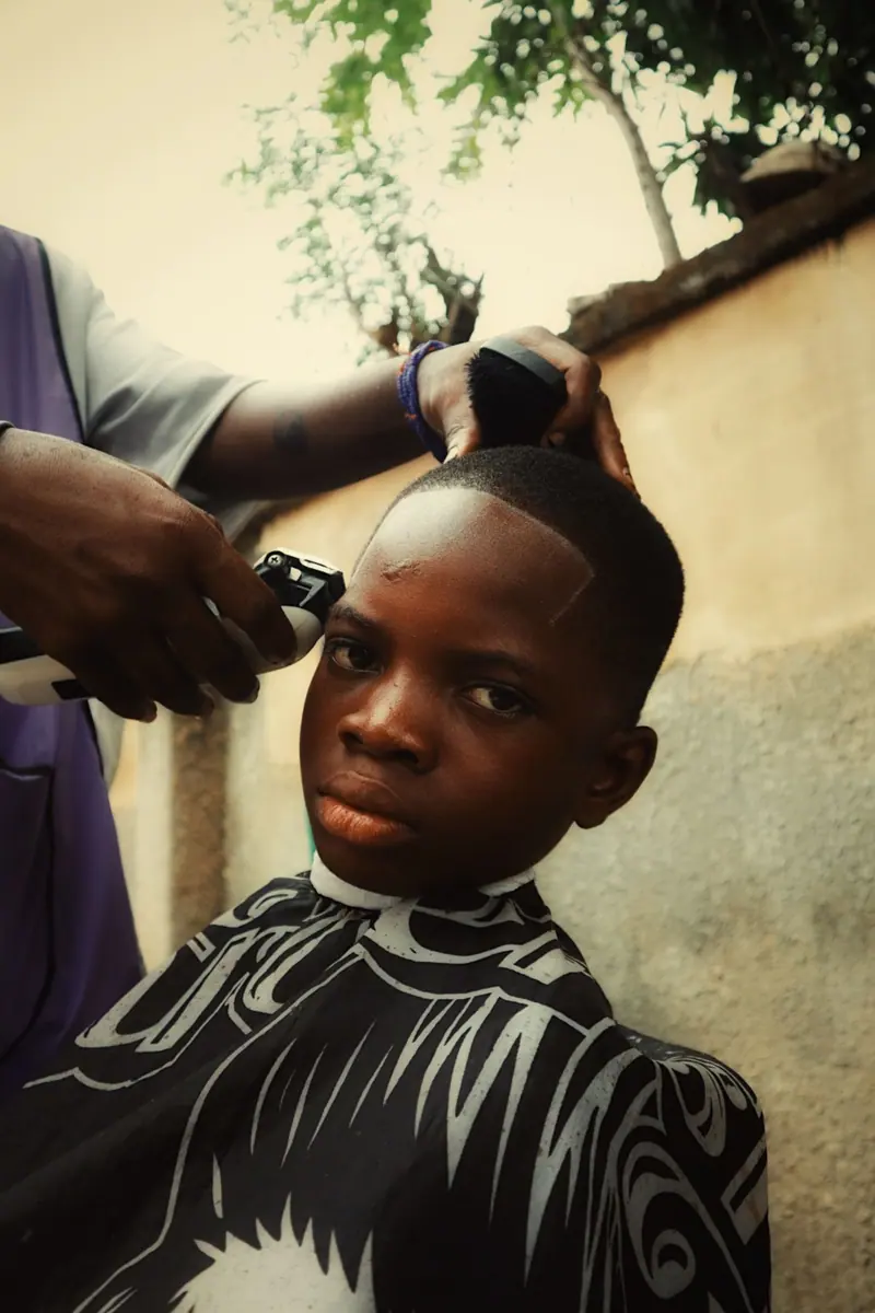 Barber giving a stylish haircut to a young boy outdoors in natural light.