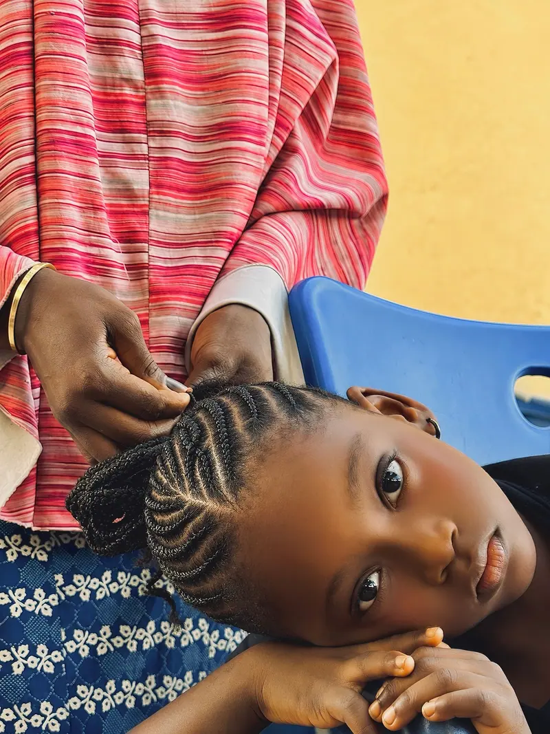 A young girl getting traditional braids. An intimate cultural moment captured.