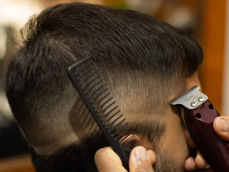 A detailed view of a man getting a haircut with clippers and a comb, showcasing precision hairstyling.
