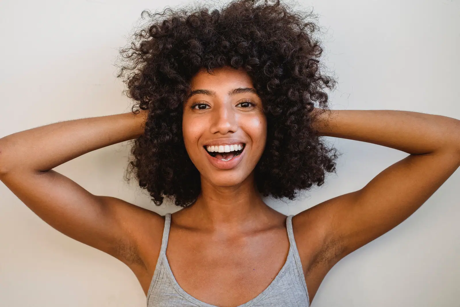 Zuri Bell laughing with her hands in her full, defined curls against a white wall