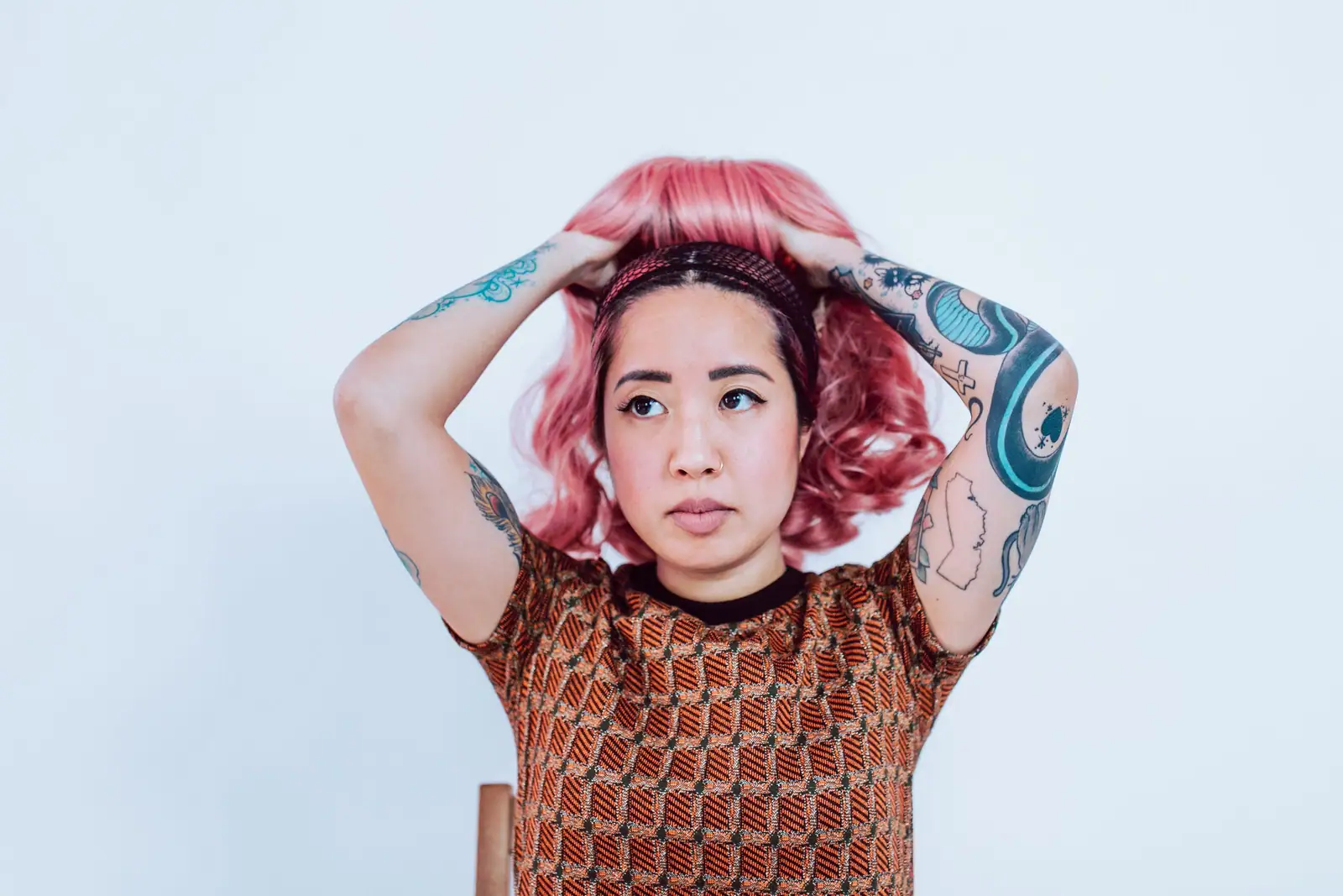 Roxy, a tattooed colorist with bright pink hair, hands on her head