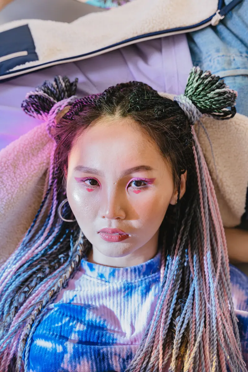 Close-up portrait of a stylish Asian woman with colorful braids and vibrant makeup.