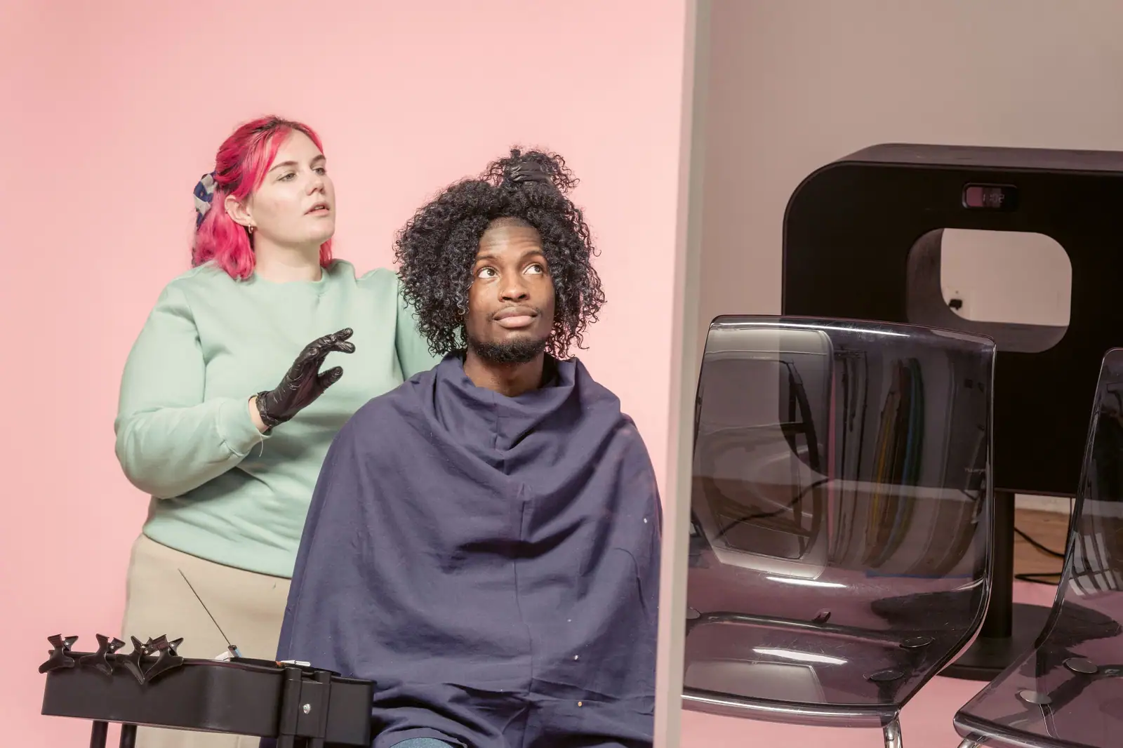 Bonnie Novak, with bright pink hair, diffusing a client’s defined curls against a pink wall