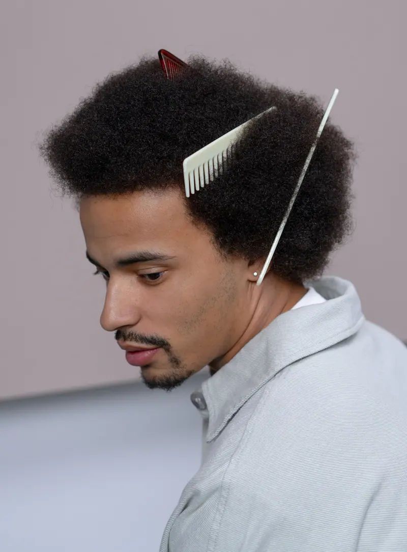 A conceptual portrait of a young man with an afro hairstyle, featuring stylish combs.