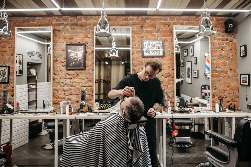 Barber working on a client's haircut in a stylish barbershop with brick walls and mirrors.